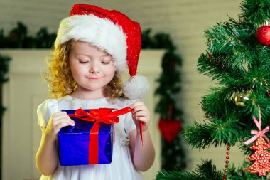 Sarışın bir kızın yakın plan portresi. Noel Baba şapkalı küçük kız. Noel mucizeleri hayal ediyor.