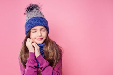 Kışın sıcacık şapkalı ve atkılı güzel küçük kız stüdyoda pembe bir arka plan üzerinde Noel hediyesini hayal ediyordu.