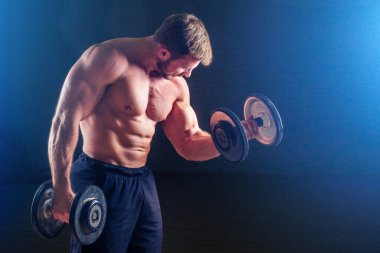 Kas geliştiren erkek fitness modeli mükemmel kaslar 6 paket karın kası ve çıplak göğüs, spor salonundaki siyah arka plan stüdyosunda halterli seksi adamla egzersiz yapıyor.