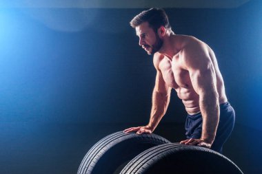 Kaslı fitness adamı, antika heykel mükemmel kaslar, altı paket karın kası ve stüdyo arka planında lastik çeviren çıplak vücut geliştirici. Fonksiyonel antrenman spor salonunu kabul et