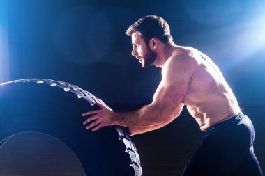 Kaslı fitness adamı, antika heykel mükemmel kaslar, altı paket karın kası ve stüdyo arka planında lastik çeviren çıplak vücut geliştirici. Fonksiyonel antrenman spor salonunu kabul et