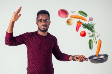 Afro-amerikan şef mutfağı elinde sihirli yemek salatası, havuç, sarımsak, soğan, biber, patates, salatalık, beyaz arka plan stüdyosu.