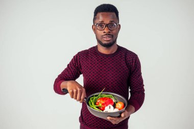 Afro-amerikan şef mutfağı elinde sihirli yemek salatası, havuç, sarımsak, soğan, biber, patates, salatalık, beyaz arka plan stüdyosu.