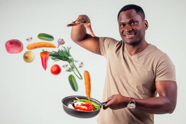 Afro-amerikan şef mutfağı elinde sihirli yemek salatası, havuç, sarımsak, soğan, biber, patates, salatalık, beyaz arka plan stüdyosu.
