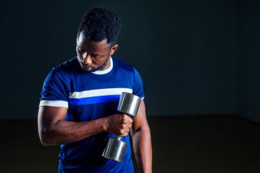 Siyah arka planda spor salonunda ağırlık kaldırarak şınav çeken kaslı Afrikalı Amerikalı bir adam.