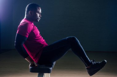 Siyah Afrikalı Amerikalı atletik adam koşu bandında koşuyor. Kas grupları üzerinde egzersiz yapıyor. Spor salonundan siyah arka planda yükseliyor.