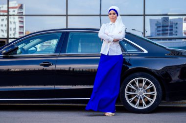 Arap iş kadını tesettür duruyor lüks arabasının önünde sokakta Dubai 'nin arka planında. Kadın şık bir abaya gibi giyinmiş.