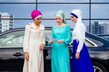 Üç başarılı çok uluslu Müslüman kadın grubu şık örtülü başörtülü bir türban başörtüsü ile baş iletişimine bağlandı ve sokak gökdeleni görünümündeki iş ofisinden bahsediyorlar.