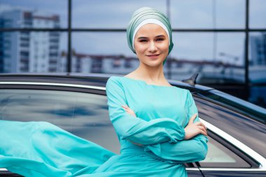 Arap iş kadını tesettür duruyor lüks arabasının önünde sokakta Dubai 'nin arka planında. Kadın şık bir abaya gibi giyinmiş.