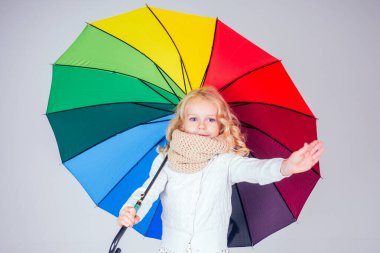 Mutlu küçük sarışın kız portresi beyaz elbiseli mavi gözlü bej örgü atkı renkli bir gökkuşağı şemsiyesi taşıyor sonbahar mevsimi stüdyoda beyaz bir arka plan çocuğu üzerinde