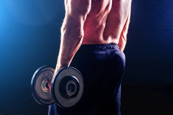 Muscular bodybuilder male fitness model doing exercises with dumbbell sexy man in the gym black background studio