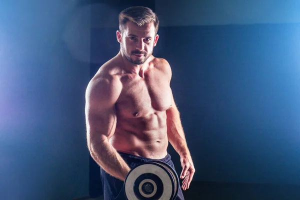 Μυώδης bodybuilder αρσενικό μοντέλο φυσικής κατάστασης τέλειους μυς έξι πακέτο abs και γυμνό στήθος κάνει ασκήσεις με dumbbell σέξι άντρας στο γυμναστήριο μαύρο φόντο στούντιο — Φωτογραφία Αρχείου