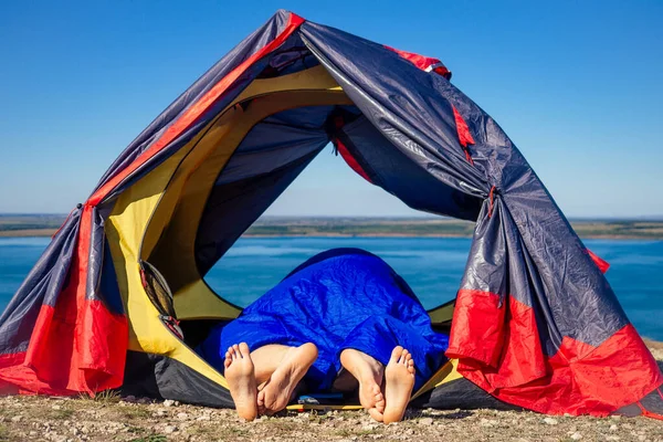 Jovem casal apaixonado na tenda escondendo o saco de dormir deitado. sexo em uma caminhada ao ar livre vista paisagem lago — Fotografia de Stock