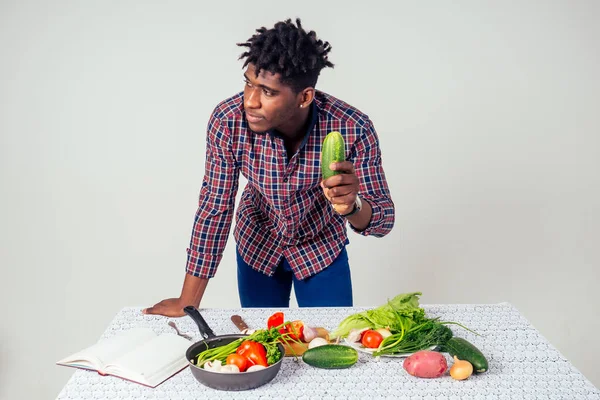 Bucătar afro-american uitându-se la cartea de rețete gătit salată gustoasă felii de legume pe masă în fundal alb în studio. meniu sănătos de alimente de casă — Fotografie, imagine de stoc