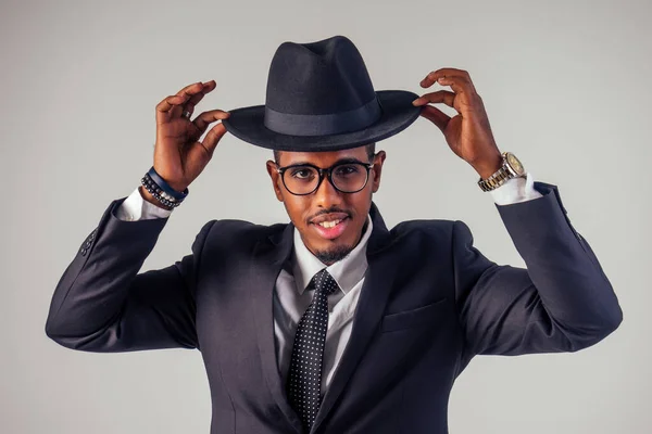 Retro style well dressed African american business man model in dark suit and black hat in studio on white background