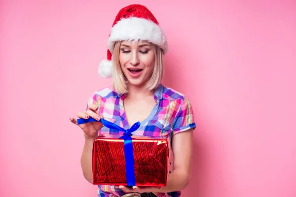 Porträtt av ung Beautyful blond förbluffad kvinna med julklapp på röd bakgrund. dam i rutig skjorta och Santa claus hålla en påse full av presenter på en rosa bakgrund i studion — Stockfoto