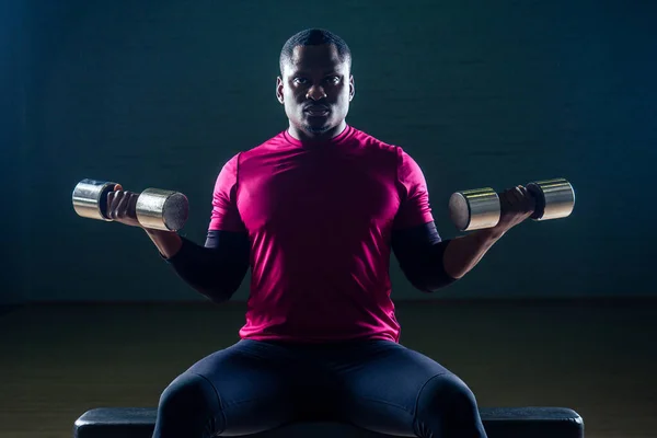 Pria Afrika berotot melakukan push-up latihan dengan dumbbell bobot di gym pada latar belakang hitam — Stok Foto