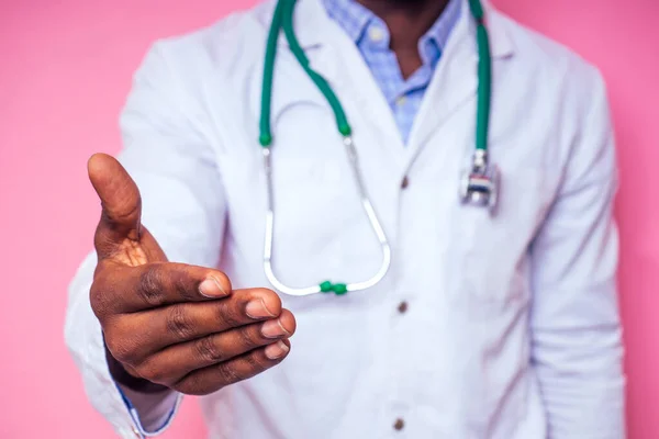 Szczęśliwy mężczyzna afrykański lekarz kardiolog lekarz w białym płaszczu wyciągając rękę na uścisk dłoni na różowym tle w studio.Witamy zaproszenie gest — Zdjęcie stockowe