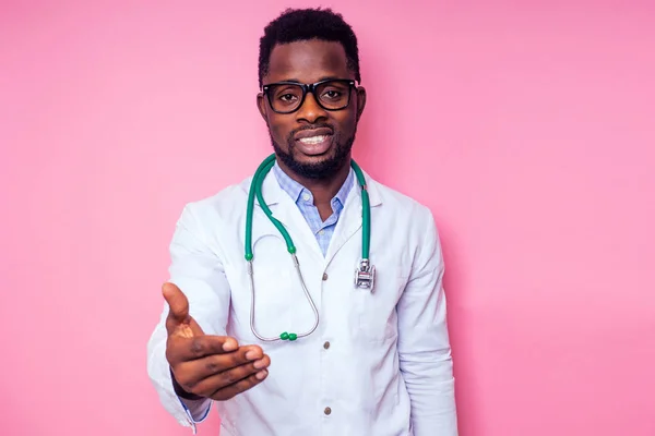 Feliz médico cirurgião médico africano masculino cardiologista médico em um casaco branco segurando uma mão para um aperto de mão em um fundo rosa no estudo.Bem-vindo gesto convite — Fotografia de Stock