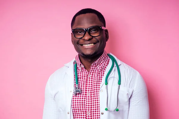 Szczęśliwy mężczyzna afrykański lekarz kardiolog lekarz w białym płaszczu na różowym tle w studio. — Zdjęcie stockowe