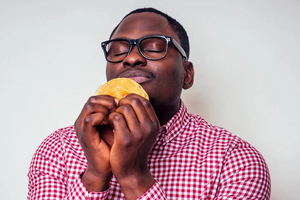 Illness sad african american man put hand on pain abdomen of hamburger.handsome and young afro man in a stylish shirt and glasses holding a burger on a white background. junk food diet indigestion