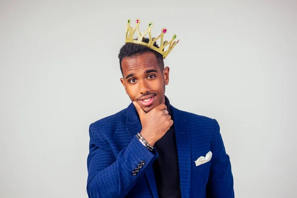 smart african american successful and rich businessman in a stylish suit and the golden crown on his head on white background in studio shot. the concept of well-deserved respect and luck