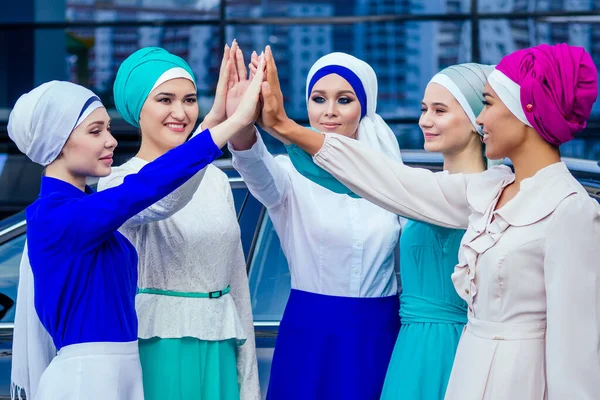 Müslüman elbiseli beş genç ve çekici iş kadınından oluşan bir grup çok renkli tesettüre ve baş parmaklarını örten bir türban merkez ekibin çalışmasında el ele tutuşuyor.