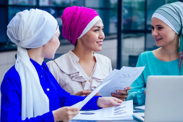 Група з трьох кавказьких мусульманських офісів обговорює з бізнес-жінкою співбесіду шаль і тюрбан на голові ідеальна шкіра і грим сидячи за круглим столом з ноутбуком і паперами. — стокове фото