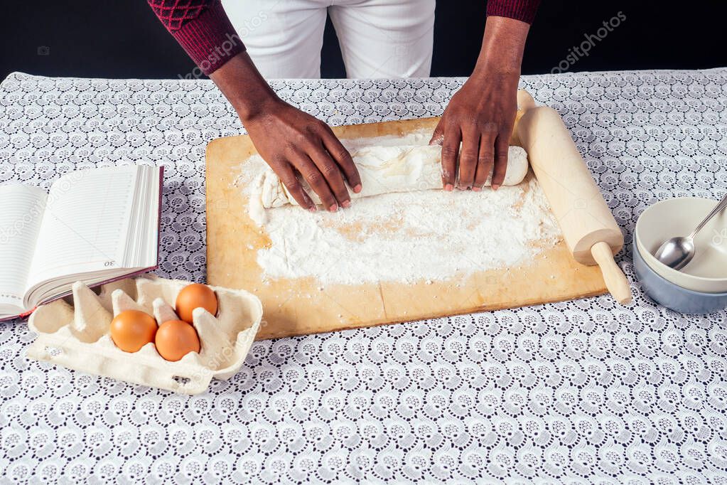 African American male cook chef boasts pastry hands in flour baking .man s hands dough rolling pin bakes cake ,eggs and recipe book on the table. homemade baking.surprise for woman on valentines day