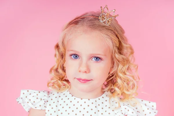 Little girl beauty queen blue eyes, curls blonde hairstyle with a tiara crown on her head in a cute white dress in peas posing in the studio on a pink background.birthday celebration,Beauty contest — Stock Photo, Image