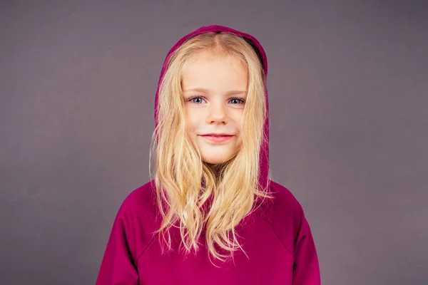 Blonde blue-eyed little model girl in a violet sports suit posing in the studio on a black background.active childhood full length portrait put on hood on head purple sporty costume hip-hop dancer — Stock Photo, Image