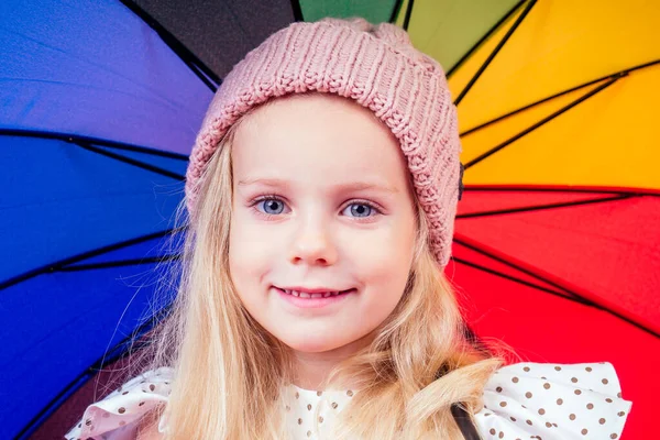 Happy funny beautiful blonde with blue eyes child with rainbow colorful umbrella in the autumn park. Girl kid playing on the nature outdoors. Family walk in the september forest yellow trees leaves — Stock Photo, Image
