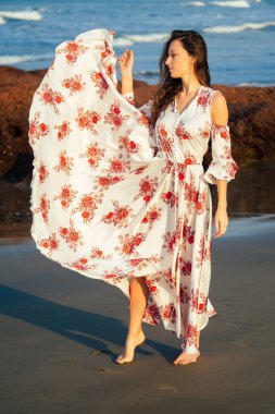 Kırmızı çiçekli, şık, beyaz elbiseli güzel bir bayan. Plaj kelebeğinin tadını çıkarıyor.