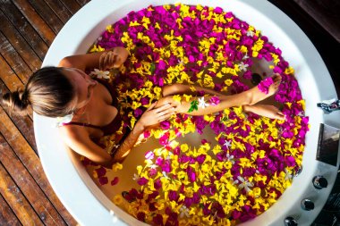 Çiçek banyosunda dinlenen genç bir kadın, organik cilt bakımı, lüks bir spa oteli. Güzellik bakımı. Yukarıdan bakıldığında, seksi, serbest kız sağlığı tedavisinde kırmızı, sarı, pembe çiçek yaprakları süt banyosunda.
