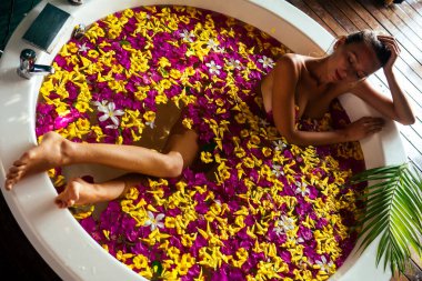 Çiçek banyosunda dinlenen genç bir kadın, organik cilt bakımı, lüks bir spa oteli. Güzellik bakımı. Yukarıdan bakıldığında, seksi, serbest kız sağlığı tedavisinde kırmızı, sarı, pembe çiçek yaprakları süt banyosunda.