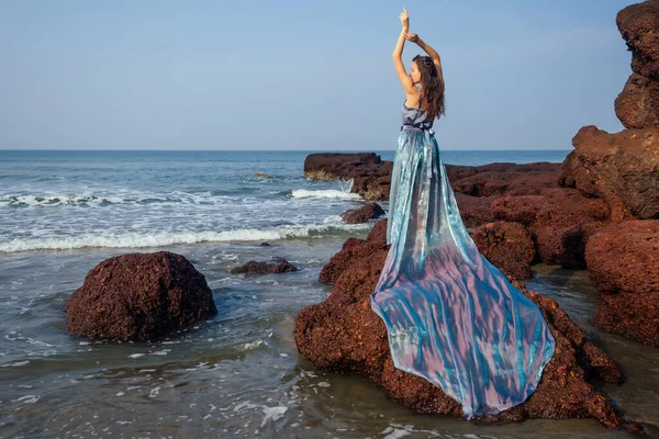 Мода красива жіноча модель позує на пляжі з камінням в довгій сукні метелика хамелеона водоспад спідниці плюм-поїзд.чуттєві парфуми з красивою і молодою брюнеткою жінкою хвилястий тропічний пісок — стокове фото