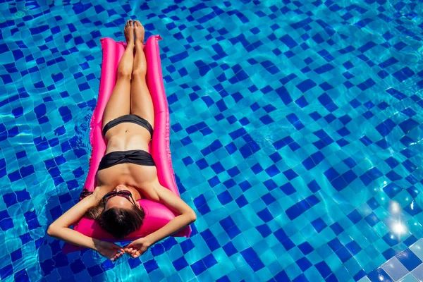 Espacio de copia spf y protector solar hermosa chica morena flotando en la piscina water.woman nadar y relajarse en el colchón inflable rosa en el trabajo remoto piscina azul y vista superior freelance — Foto de Stock