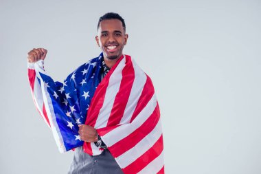 Afrikalı Amerikalı bir adam kameraya bakıyor ve gururla stüdyoda Amerikan bayrağı tutuyor.