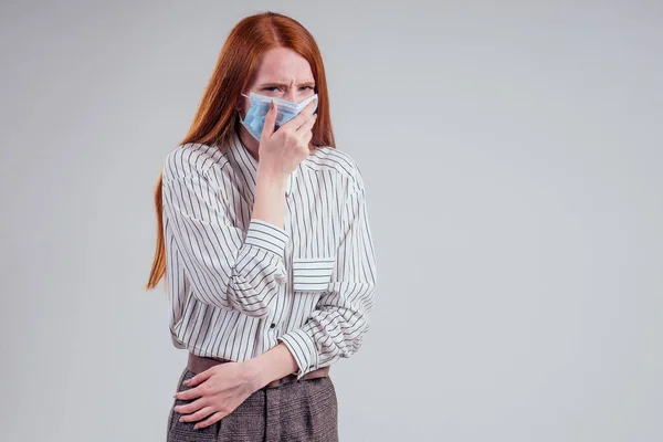 Mujer pelirroja infeliz ojos verdes empresarias en una camisa a rayas con gasa máscara azul fondo blanco estudio — Foto de Stock