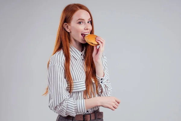 Rothaarige hungrige Frau in gestreiftem Hemd isst USA Burger Visum Reisender weißen Hintergrund Studio — Stockfoto