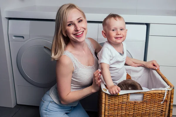 Mutlu aile evi hafta sonu sabah banyo yıkama makinesi. Anne ve küçük oğlu çamaşır odasında çamaşır yıkıyor. — Stok fotoğraf