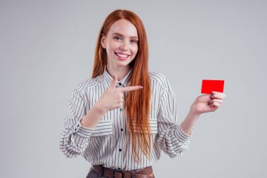 Çekici kızıl saçlı beyaz iş kadını çizgili tişört giyiyor kredi kartı stüdyosu beyaz arka plan kara cuma indirimi nakit para taşıyor.