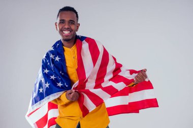Afrikalı Amerikalı bir adam kameraya bakıyor ve gururla stüdyoda Amerikan bayrağı tutuyor.