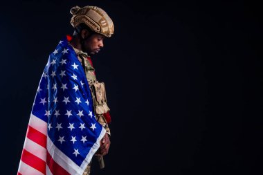 Askeri ordu Afrikalı erkek kamuflaj kıyafeti. Amerikan bayrağına sarılı. Üzüntü siyah arka plan stüdyosu.