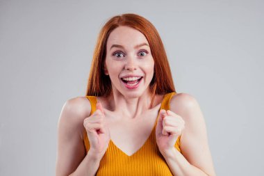 Mutlu, kızıl saçlı, mükemmel tenli, sarı gömlekli, neşeli ve büyüleyici kar beyazı tebessümü stüdyosunun arka planında kameraya bakan genç kadın..