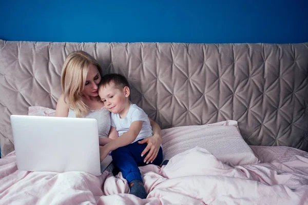 Madre e hijo se divierten mientras están sentados con el ordenador portátil en la cama — Foto de Stock