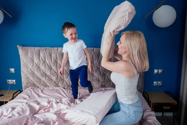 Aile hafta sonu birlikte eğleniyor. Anne ve çocuk yatakta. Sarışın anne ve bebek sabah yatak odasında yastık savaşı yapıyorlar. Ebeveyn ve küçük çocuk evde dinleniyor. Anneler Günü — Stok fotoğraf