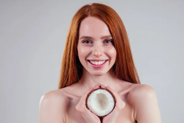 Kızıl saçlı, mükemmel tenli, kızıl saçlı genç bir kadın beyaz stüdyo arka planında hindistancevizini elinde tutuyor.. — Stok fotoğraf