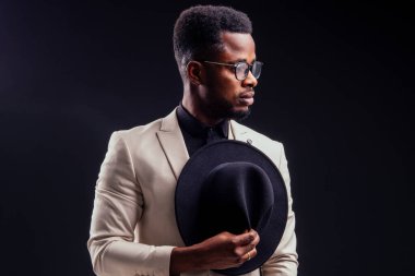 Beyaz ceketli, gözlüklü, stüdyodaki siyah arka planlı yakışıklı Afro-Amerikan melankolik çocuk. Gizem ve keder.