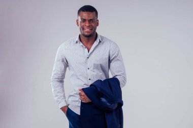 Siyah pantolonlu ve ceketli şık bir Afro-Amerikalı stüdyoda beyaz arka planda poz veriyor.